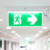 A Arrow light box sign of EMERGENCY FIRE EXIT is hung on the ceiling in hospital walkway, Idea for event fire or evacuation drills.